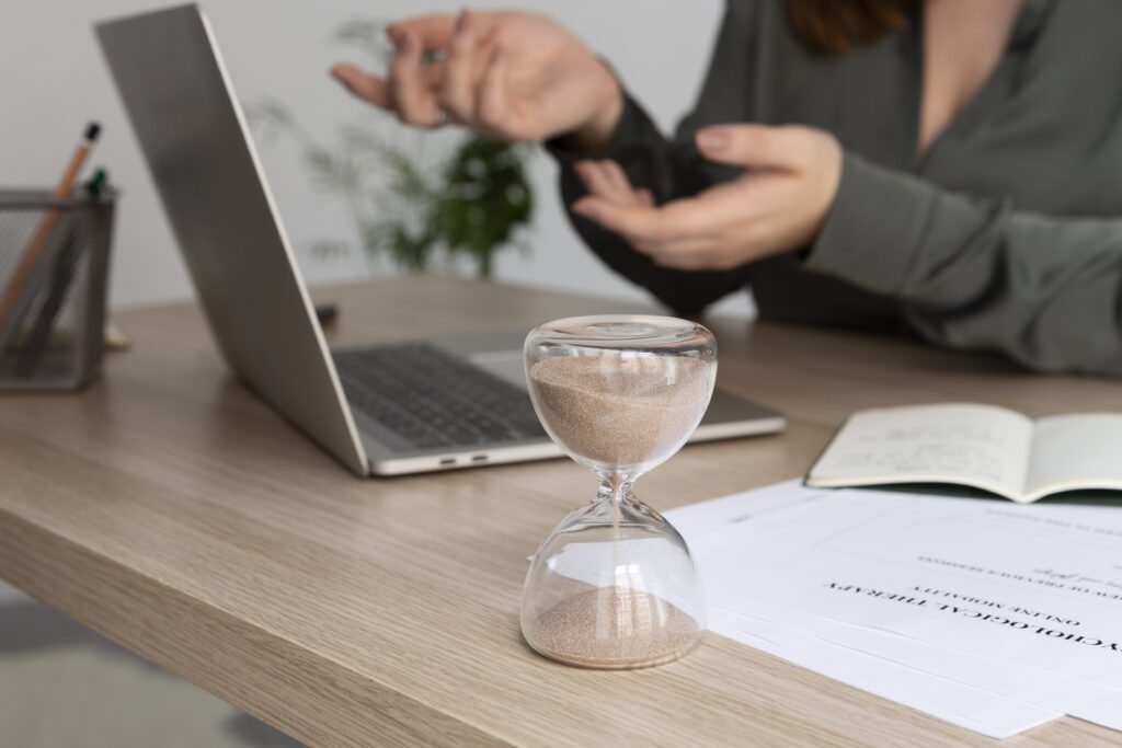 Person conducting online therapy session with laptop, hourglass, and notes on unpaid overtime and legal rights.