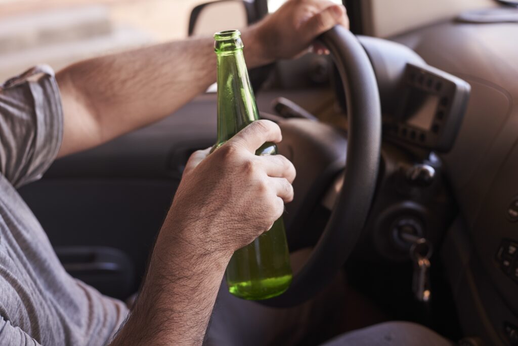 Man holding a green beer bottle while driving a car, highlighting the dangers of DUI and the importance of legal defense in Georgia.