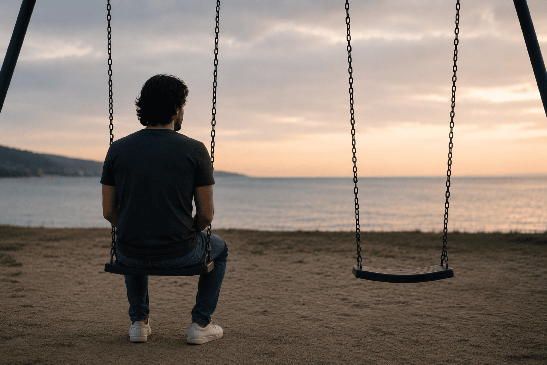A person sitting alone beside an empty swing at dusk, reflecting the loss of a loved one