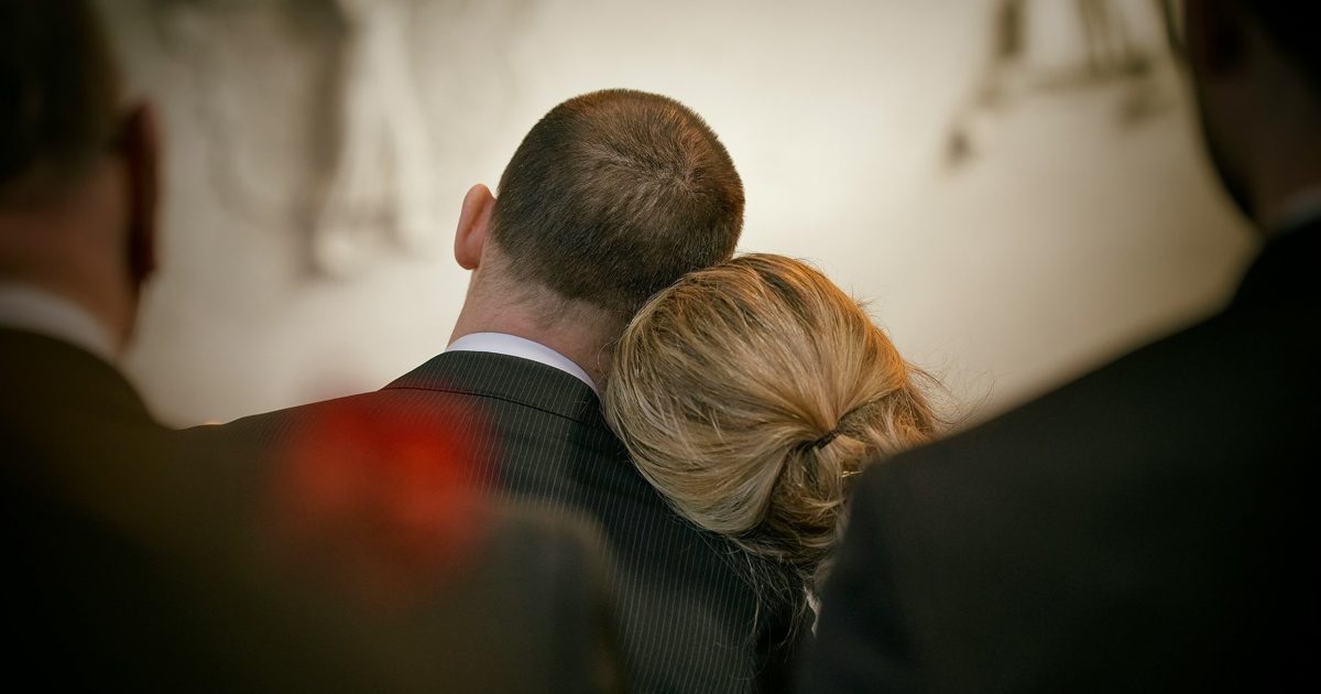 Grieving couple embracing at a memorial service after a family member's workplace death